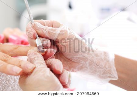 Removing the hybrid paint using a chisel.
Beautician scratches the nail varnish of the client.