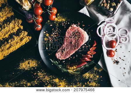 Raw meat with spices, cherry tomatoes, pepper, onion and olives, lying on black background and white napkin. Cooking delicious dinner for party or a romantic evening for two lovers. unbelieveble tasty