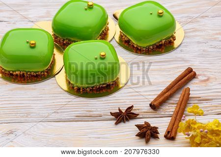 Delicate green three-layer mousse with. cinnamon sticks over a white wooden board.