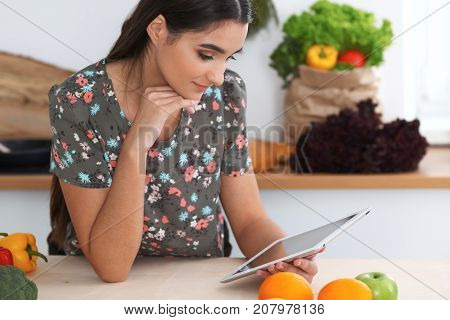 Young hispanic woman is making online shopping by tablet computer and credit card. Housewife found new recipe for cooking in a kitchen.