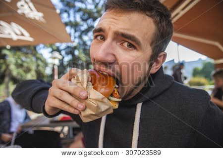 A Guy Is Looking At The Camera With The Eyes Full Of Dissapointment. He Is Eating His Hamburger. Bad