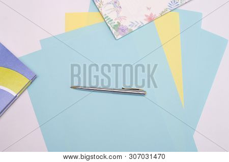 Ballpoint Pen Lies On Sheets Of Blue And Yellow Paper Next To The Notebook, White Background, Layout