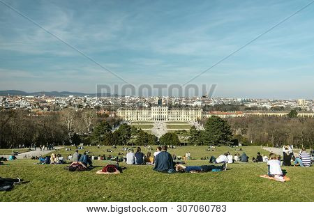 Viena, Austria - March 18, 2019: People Sitting On The Lawn On The Schonbrunn Palace Background