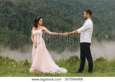 Beautiful Young Wedding Couple Standing On The Green Slope, Hill. Groom And Bride In Carpathian Moun