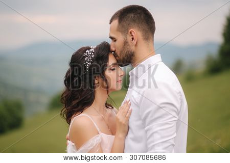 Beautiful Young Wedding Couple Standing On The Green Slope, Hill. Groom And Bride In Carpathian Moun