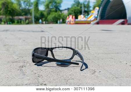Broken Sun Glasses Lie On A Stone Tiled Walkway In The City Park Against The Background Of Residenti