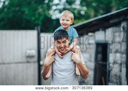 Blonde Three Years Old Boy Sitting On Father's Shoulders. Kazakh Father And Caucasian Mother. Happy 