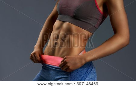Close Up Of Womans Abs With Tanned Skin And Hands On Hips. Female With Perfect Abdomen Muscles Posin