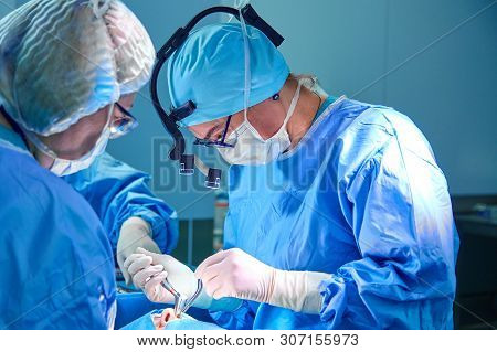 Surgeon And His Assistant Performing Cosmetic Surgery In Hospital Operating Room. Surgeon In Mask We