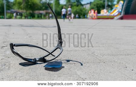 Broken Sun Glasses Lie On A Stone Tiled Walkway In The City Park Against The Background Of Residenti