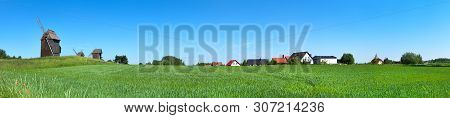 Rural Landscape In Poland. Panoramic Image With Historical Windmill And Roofs Of Rural Houses Behind