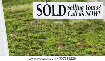 A White Sold Sign With Black Letters Hanging Over Grass With Room For Copy Spce Underneath.