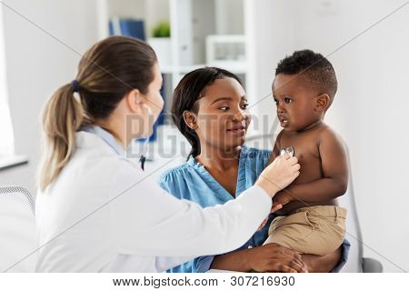 medicine, healthcare and pediatry concept - doctor with stethoscope listening to african american baby boy on medical exam at clinic