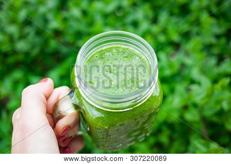 woman's hand holding a jar with green cold-pressed juice, nature background. Healthy eating, detoxing, juicing, body cleancing concept 