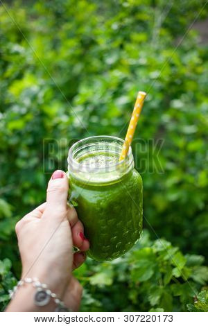 woman's hand holding a jar with green cold-pressed juice, nature background. Healthy eating, detoxing, juicing, body cleancing concept 