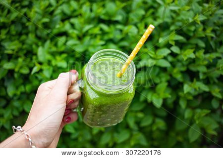 woman's hand holding a jar with green cold-pressed juice, nature background. Healthy eating, detoxing, juicing, body cleancing concept 