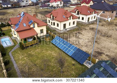 Aerial Top View Of Residential Area With New Houses With Roof Solar Photo Voltaic Panels, Wind Turbi