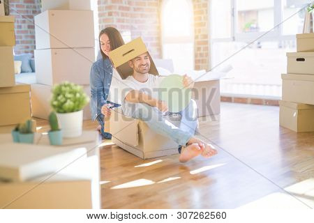Funny and crazy couple having fun riding a cardboad box as a car, smiling happy and lauging at new home