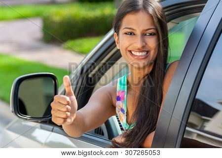 Beautiful Indian Asian young woman or girl leaning out of a car giving a thumbs up in summer sunshine smiling with perfect teeth and long hair. Car hire, driving test concept.