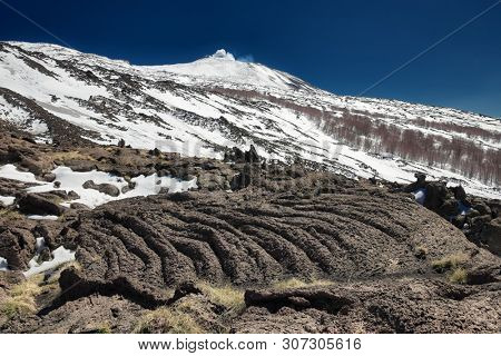 cooled lava flow ropy surface, on background winter Etna Volcano, Sicily