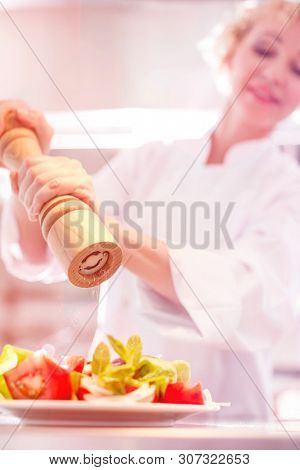 Mature chef using peppermill on salad in plate at restaurant