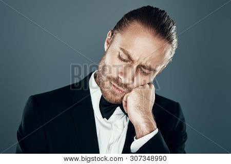 Sick And Tired. Charming Young Man In Bow Tie In Full Suit Leaning On His Hand While Standing Agains