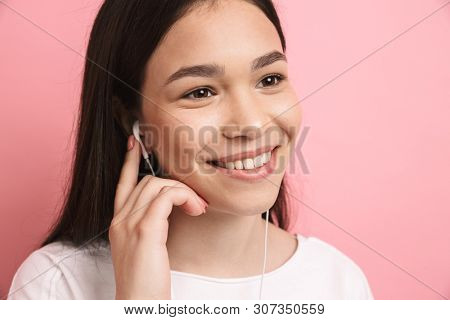 Portrait closeup of optimistic pretty girl wearing earphones smiling while listening to music isolated over pink background