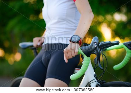 Multisport Smartwatch on the Hand of Young Woman Road Cyclist Resting with Bicycle at Sunset. Closeup of Hand with Fitness Tracker. Training and Sports Concept.