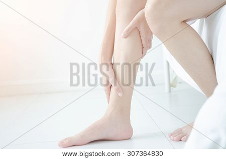 Asian Girl Wearing White Dress Have Leg Pain. The Woman Was Squeezing Her Leg In A White Bedroom Wit