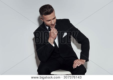 Looking Just Perfect. Handsome Young Man In Full Suit And Bow Tie Keeping Hand On Chin And Smiling W