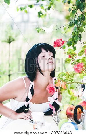 Alice In Wonderland. The Girl With Dark Long Hair Inhales The Fragrance Of A Flower. The Tale, A Par