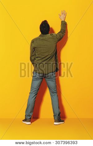 A full length portrait of a fashionable young man posing in the studio with the back over the yellow background. Casual fashion for men.