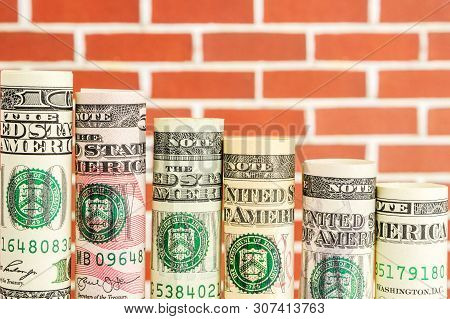 Declining Steps Made Of Rolls Of All American Dollar Banknotes In One Row On Red Brick Wall Backgrou
