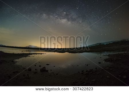 The Stars In The Sky Reflect The Light At Night. The Milky Way Above The Mountains And The Pond Mae