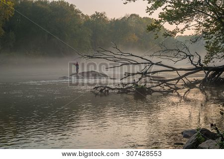 A Fisherman Fly Fishing In The Early Morning Fog As The Sunrises Standing On A Rock In The Chattahoo