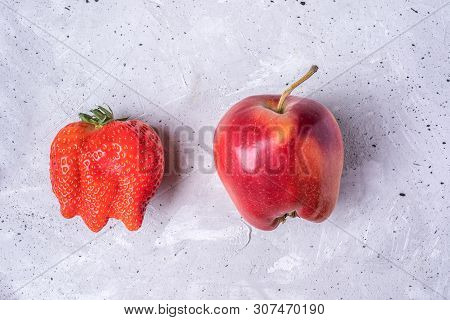 Two Ugly Fruits: Strawberry And Apple On Grey Concrete Background.