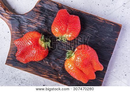 Close-up Three Ugly Strawberries On Burned  Board On Concrete Background.