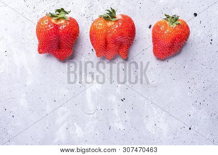 Three Ugly Red Strawberries On Grey Concrete Background.