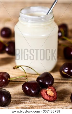 Greek Yoghurt With Spoon, Opened Cherry With A Ossicle, On A Cherryes And Brown Wooden Background