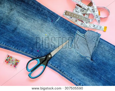 Folded In A Half Blue Jeans With Large Hole On Pant Leg Below The Knee, Multi Coloured Headed Sewing