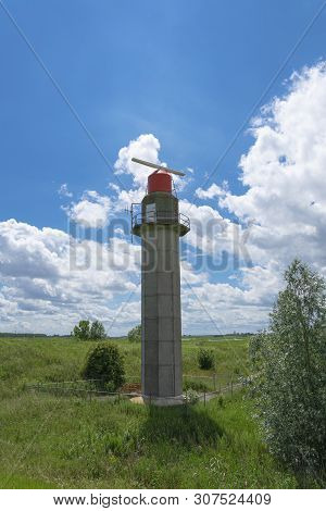 Radar Tower In Ancients Doel, Belgium With A Red Top In Green Surroundings And A Cloudy Blue Sky