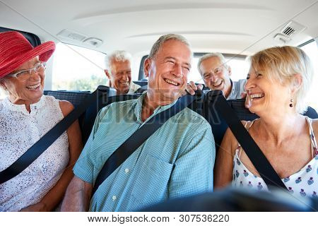 Group Of Senior Friends Sitting In Back Of Van Being Driven To Vacation