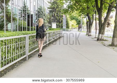 Slender Girl Student With A Backpack Goes On The Sidewalk Along The Fence To The University