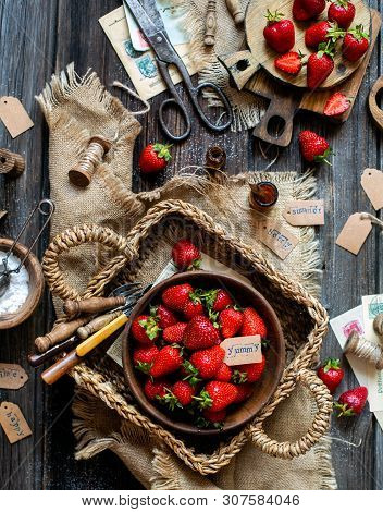 Overhead Shot Of Tasty Ripe Strawberries In Wooden Bowl Stands In Wicker Strawy Basket On Rustic Tab