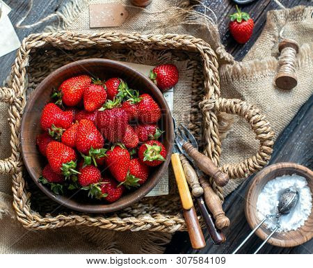 Overhead Shot Of Tasty Ripe Strawberries In Wooden Bowl Stands In Wicker Strawy Basket On Rustic Tab