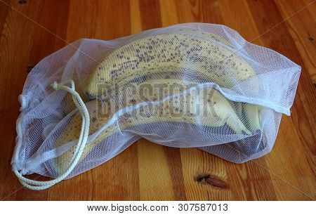 Bunch of bananas packed in a reusable mesh bag on a wooden background. Eco-friendly packaging. Close-up. Indoors.