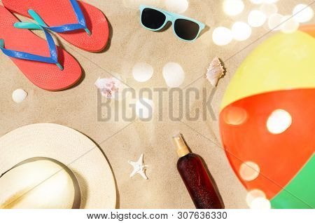 vacation and summer holidays concept - straw hat, flip flops, sunglasses, beach ball and sunscreen oil with seashells on sand