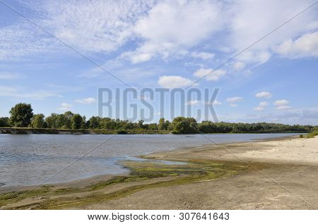 Wide Blue River Is Slow Flowing. Summer. Sunny Weather And White Sand. Green Trees Far Away