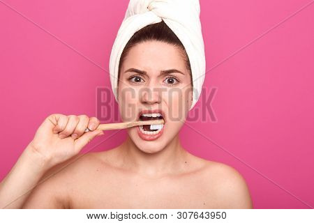 Indoor Studio Shot Of Displeased Energetic Young Woman Looking Directly At Camera, Brushing Teeth In