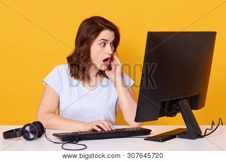 Indoor Shot Of Brunette Woman Using Computer, Cheking Her Social Networks, Reading Shocking Informat